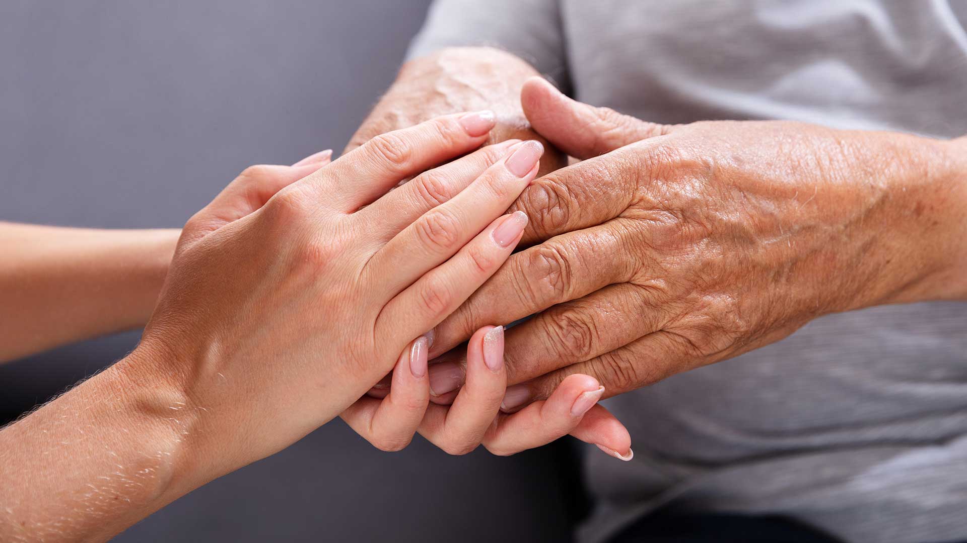 A carer's hands gently supporting an elderly client